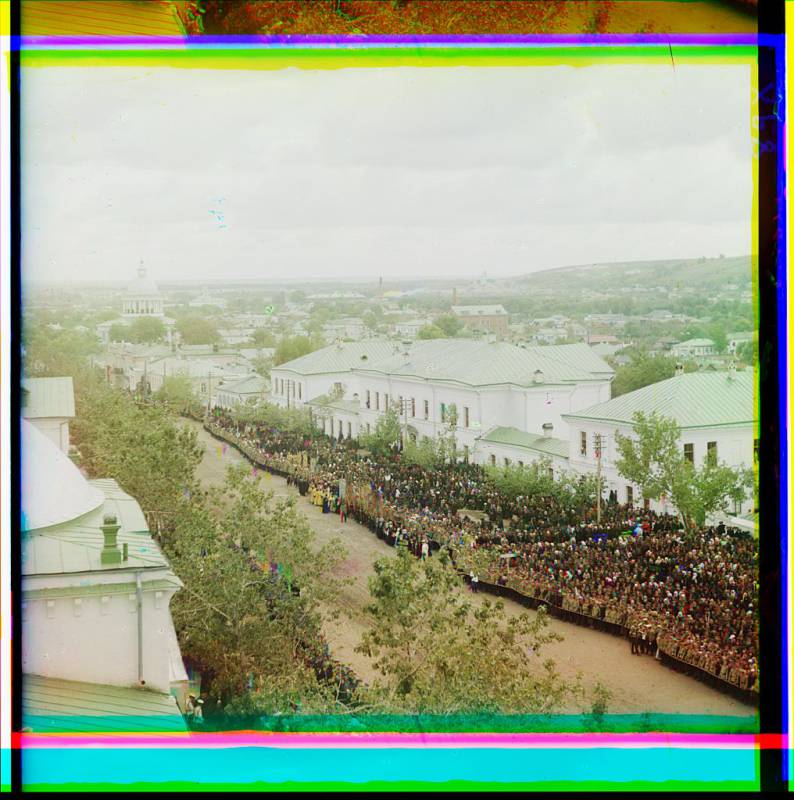 crowd_of_people_assembled_beside_roadway_domed_building_and_town_in_background.jpg