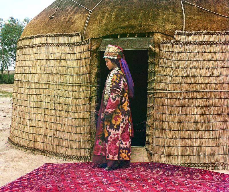 full-length_profile_portrait_of_a_woman_possibly_turkman_or_kirgiz_standing_on_a_carpet_at_the_entrance_to_a_yurt_dressed_in_traditional_clothing_and_jewelry.jpg