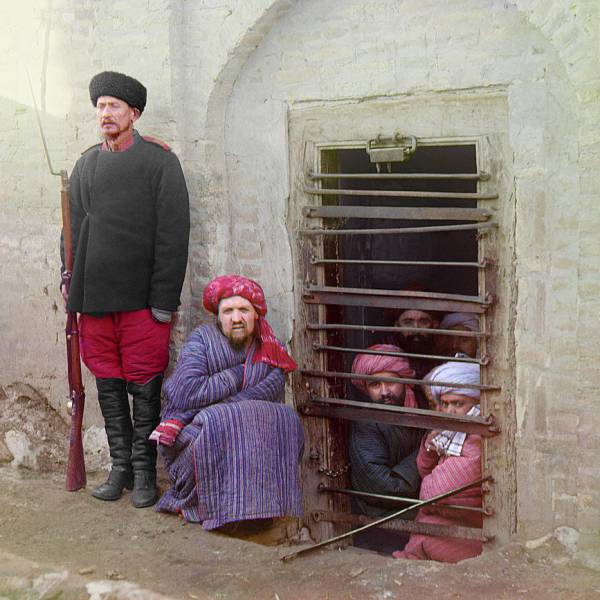 zindan_prison_with_inmates_looking_out_through_the_bars_and_a_guard_with_russian_rifle_uniform_and_boots_central_asia._2.jpg