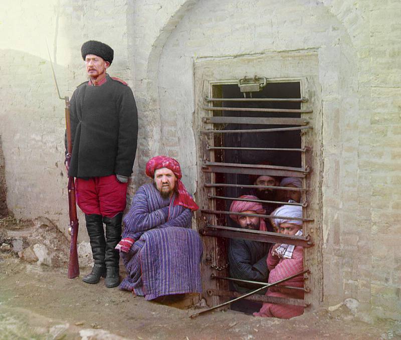 zindan_prison_with_inmates_looking_out_through_the_bars_and_a_guard_with_russian_rifle_uniform_and_boots_central_asia._2.jpg